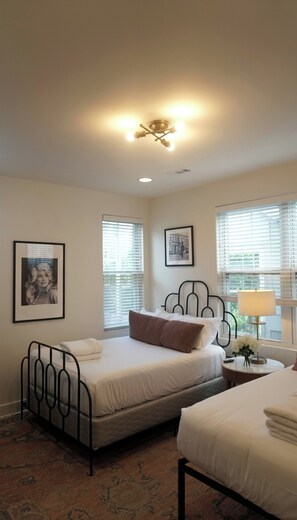 A hotel room with a bed, a bedside table with a lamp, a framed picture on the wall, and a window with blinds. - Sleeps 8 near Broadway — Hart Suites Unit #6 (Nashville)