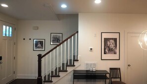 A staircase with a wooden handrail and white balusters, leading to a landing with a framed picture and a table with chairs. - Sleeps 8 near Broadway — Hart Suites Unit #6 (Nashville)