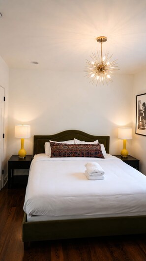 Ein Hotelzimmer mit einem Bett, zwei Nachttischen, einer modernen Chandelierleuchte und einem gerahmten Bild an der Wand.