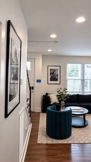 A modern living room with a staircase, a black sofa, a teal ottoman, and a coffee table. - Free parking near Broadway — Hart Suites #7 (Nashville)