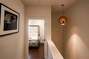Ein Flur mit einem Bett im Hintergrund, einem gerahmten Bild an der Wand und einer Pendelleuchte.