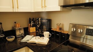 Una cocina con tostadora, cafetera y hervidor. Hay utensilios y un tazón de arándanos.