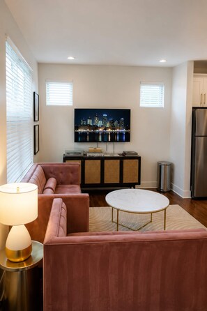 A modern living room with a sofa, a coffee table, and a television mounted on the wall. - 10 Min to Broadway | Sleeps 8 | Hart Suites #16 (Nashville)