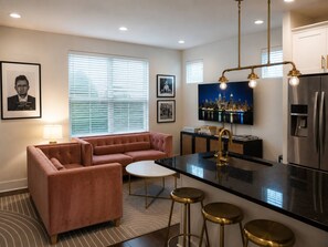 A modern kitchen with a central island, bar stools, a sofa, and a television. - 10 Min to Broadway | Sleeps 8 | Hart Suites #16 (Nashville)