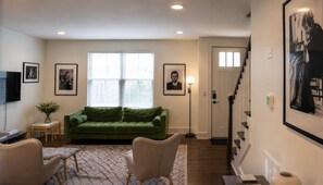 A living room with a green sofa, two armchairs, a TV, and framed pictures on the walls. - Spacious townhome, sleeps 8 — Hart Suites #8 (Nashville)