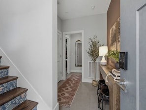 A hallway with a wooden staircase, a rug, a plant, a lamp, and a door with a keypad lock. - Luxury 3BR Retreat | Minutes from Broadway (Nashville)
