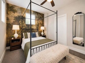 A four-poster bed with a green bedspread, two bedside lamps, a fluffy white bench, a ceiling fan, and a large mirror on the wall. - Luxury 3BR Retreat | Minutes from Broadway (Nashville)