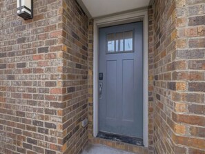 A grey door with a small window above it, set in a brick wall. - Luxury 3BR Retreat | Minutes from Broadway (Nashville)