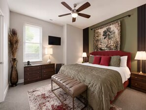 A bedroom with a bed, a bench, a ceiling fan, a TV, and a painting on the wall. - Luxury 3BR Retreat | Minutes from Broadway (Nashville)