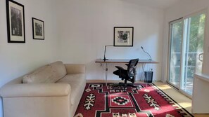 A room with a sofa, a desk with a chair, and a large window.