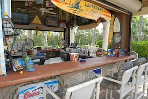 A bar area with a counter, seating, and various items like a Coors beer sign, a fan, and a surfboard decoration. - Luxury 8 Bedroom Villa, Pool/Spa (Kissimmee)