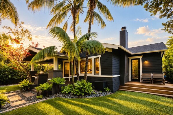 A modern house with a dark exterior, a well-maintained lawn, and a patio area with chairs. - Luxury 1913 Craftsman in Venice Beach (Los Angeles)