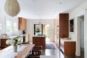 A modern kitchen with wooden cabinets, a central island, and a dining area with a table and chairs. - Luxury 1913 Craftsman in Venice Beach (Los Angeles)