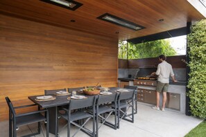 An outdoor kitchen with a grill, dining table, and chairs. - Luxury 1913 Craftsman in Venice Beach (Los Angeles)