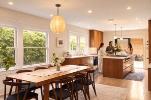 A modern kitchen with a central island, wooden cabinets, and a dining area with a table and chairs. - Luxury 1913 Craftsman in Venice Beach (Los Angeles)