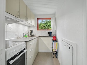 A compact kitchen with white cabinets, a stove, a sink, and a window overlooking greenery. - "Mea" - 750m from the sea by Interhome (Væggerløse)
