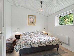 Een slaapkamer met een bed, bedlampen, een raam met uitzicht op groen en een ingelijste foto aan de muur.