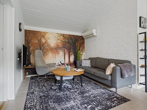 A modern living room with a sectional sofa, a grey armchair, a coffee table, and a large wall mural of a forest scene. - "Mea" - 750m from the sea by Interhome (Væggerløse)