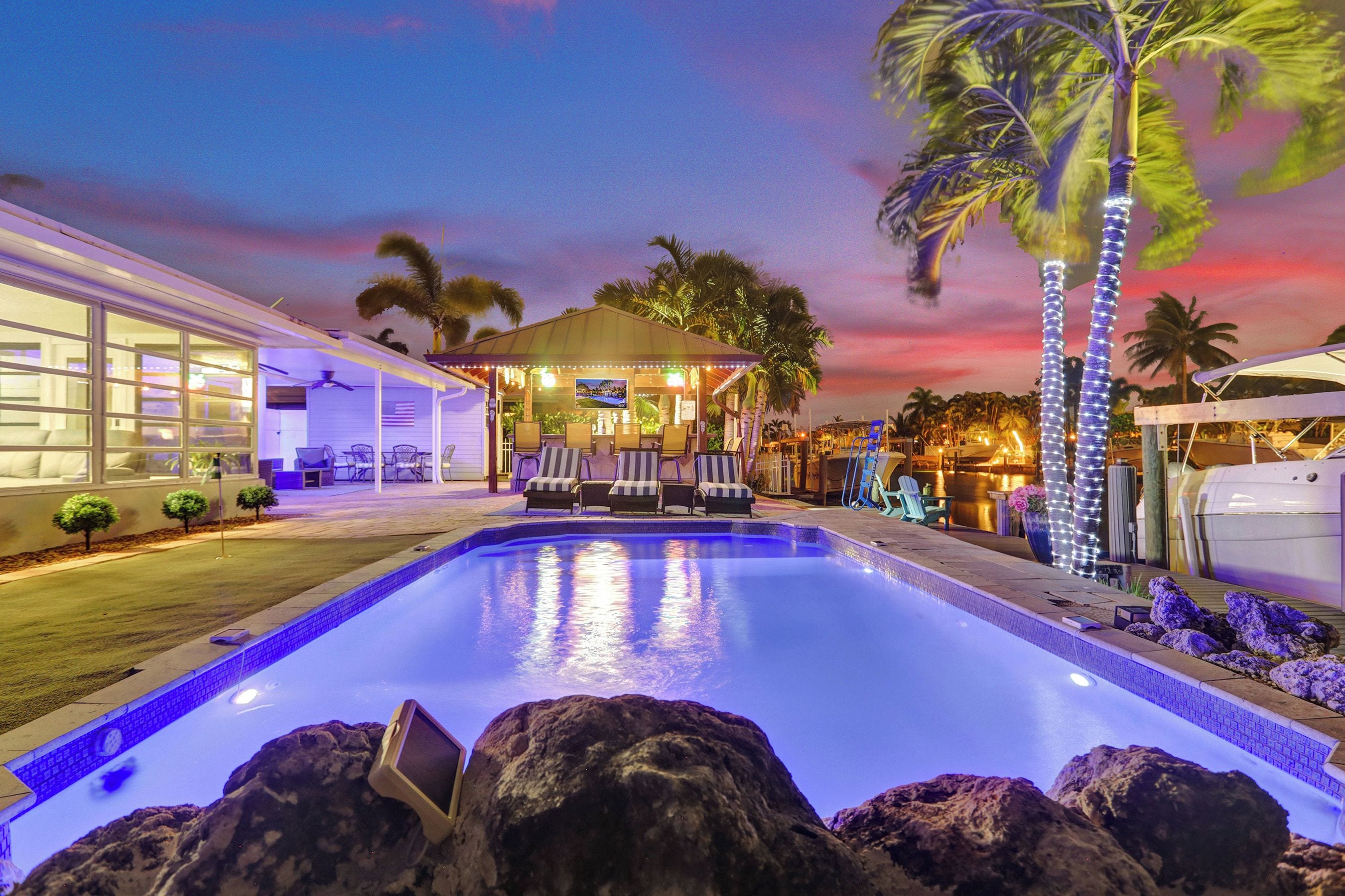 A swimming pool with lounge chairs, a covered seating area, and palm trees.