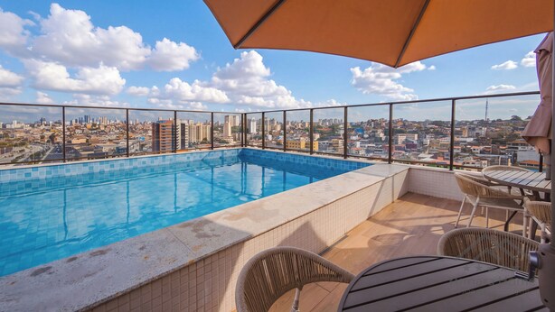 Una piscina en la azotea con vista a la ciudad, rodeada de mobiliario exterior.