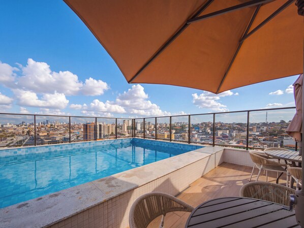 Una piscina en la azotea con vista a la ciudad, rodeada de mobiliario exterior.