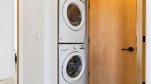 A laundry room with two stacked washing machines and a wooden door. - Cielo Vista by Avantstay Private Pool + Heated Spa Pickleball Court Fire Pit Near the Park (Joshua Tree)