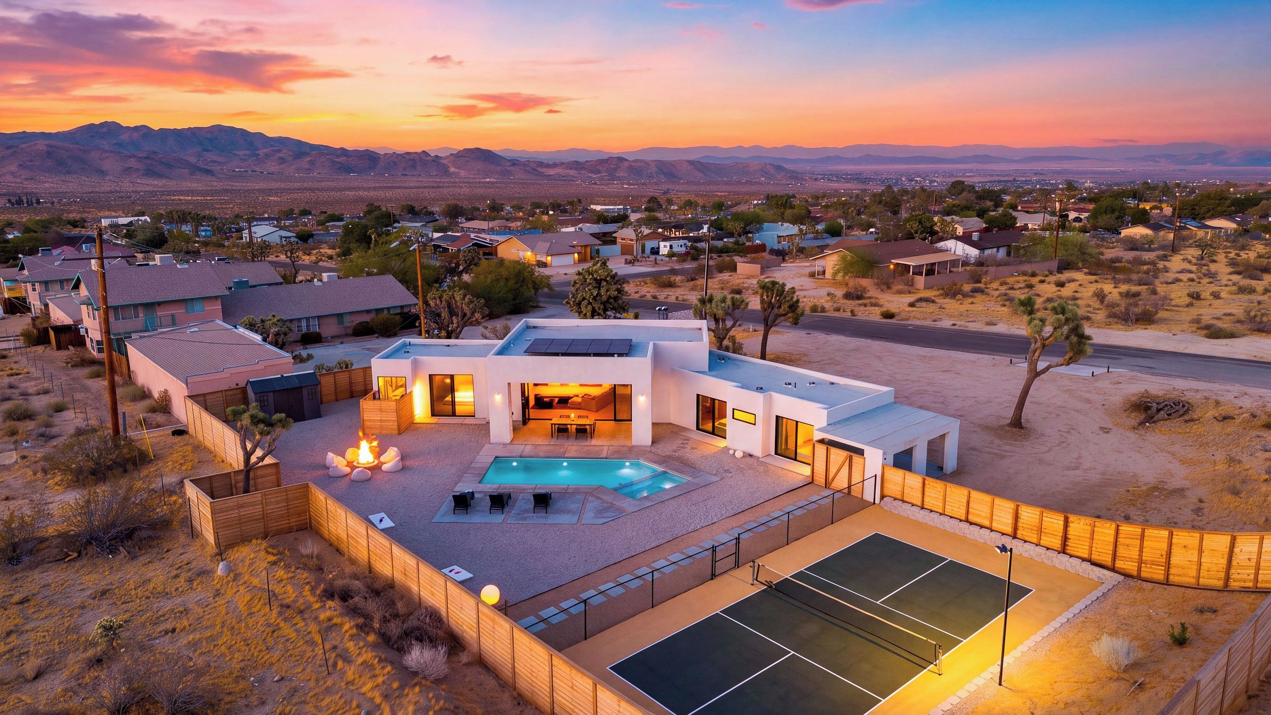 A modern house with a swimming pool, tennis court, and a view of the desert landscape.