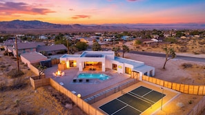 A modern house with a swimming pool, tennis court, and a view of the desert landscape.