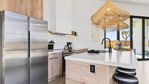Una cocina moderna con una isla grande, electrodomésticos de acero inoxidable y una lámpara colgante de fibras.
