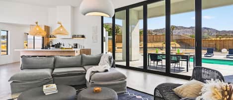 A modern living space with a sectional sofa, a round coffee table, and a dining area with a pool view.
