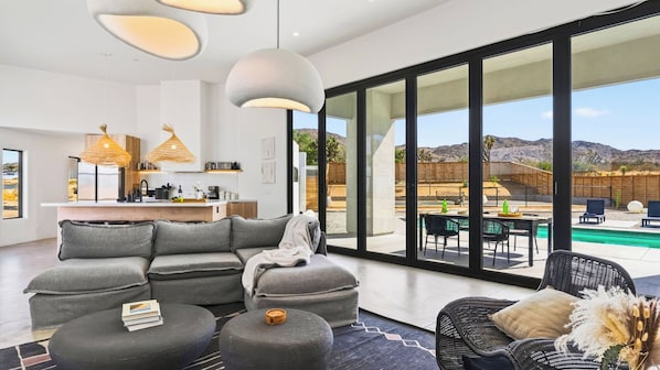 A modern living space with a sectional sofa, a round coffee table, and a dining area with a pool view.