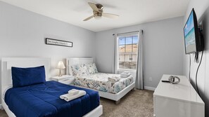 A bedroom with a bed, a nightstand, a desk, a ceiling fan, a TV, and a window with blinds. - Enchanting 4BR Villa / Family Vacation Home Near Disney (Kissimmee)