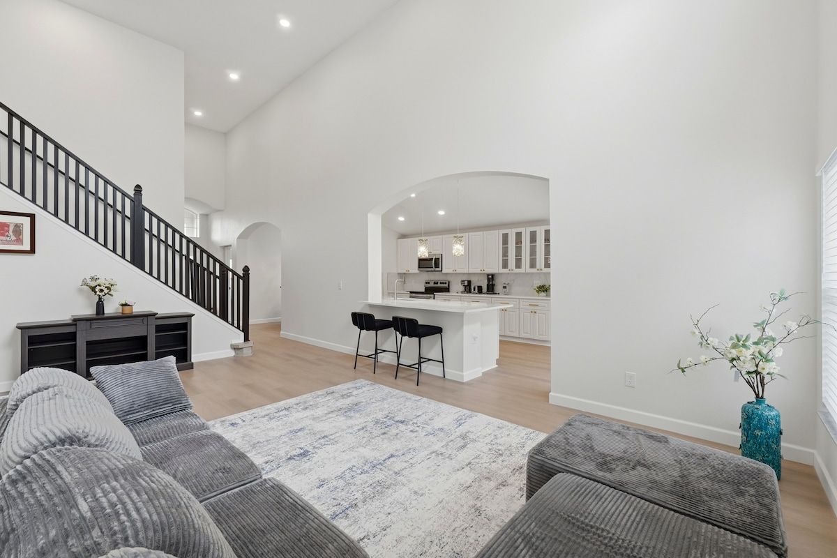 Amplia sala de estar con escalera, cocina con isla y zona de estar con otomanas.