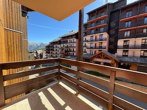 A wooden balcony with a view of a mountain range and a hotel building with multiple balconies and a sign reading 'INTERSPORT'. - Séjour montagne - 6 pers avec balcon à Risoul (Risoul)