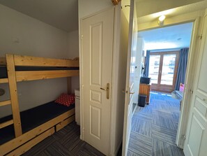 Une pièce avec un lit superposé, une porte et un couloir menant à un espace extérieur.