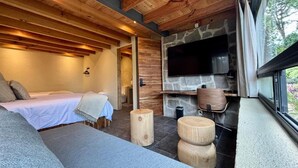 A cozy room with a bed, a stone fireplace, and a large window. - Pandurata Bed & Breakfast (Valle de Bravo)