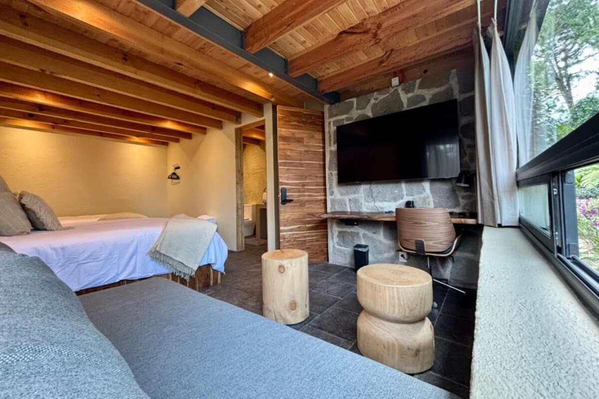 A cozy room with a bed, a stone fireplace, and a large window.