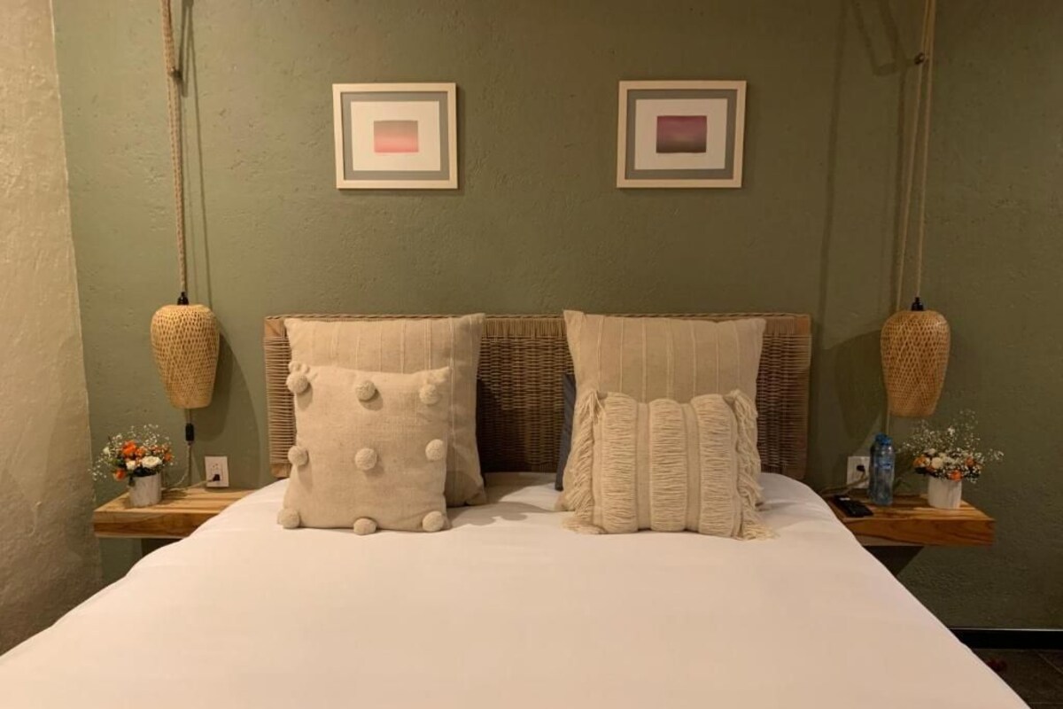 A bed with two pillows, a bedside table with a vase and a lamp, and two framed pictures on the wall.