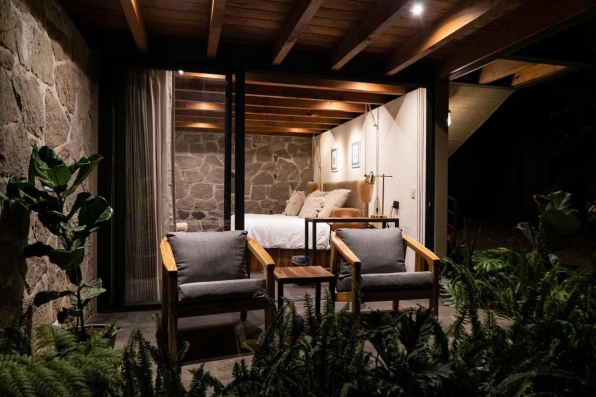 A cozy room with a stone wall, a bed with pillows, a wooden bench, and a table.