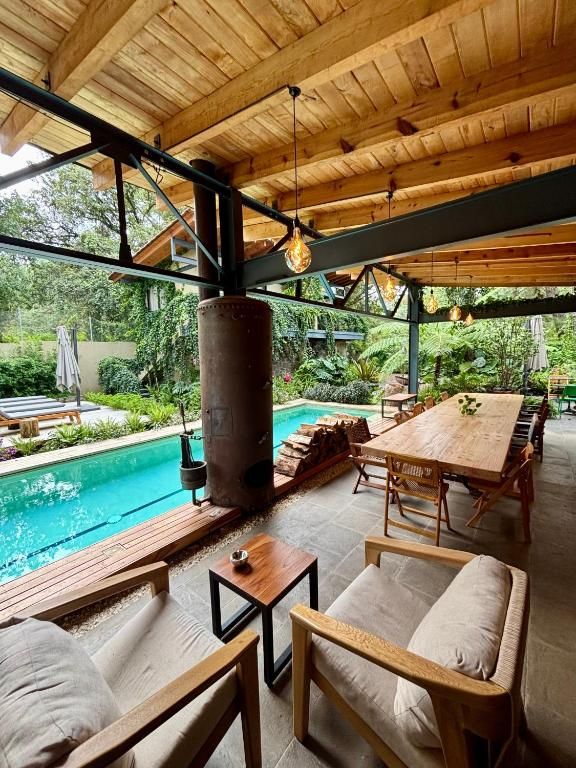 Un espacio de estar al aire libre con piscina, mobiliario de madera y vistas al entorno verde.