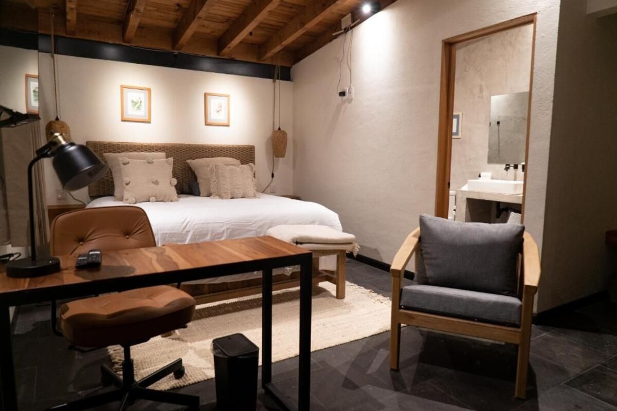 A bedroom with a bed, bedside table, lamp, chair, and a mirror.