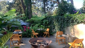 An outdoor seating area with a fire pit, surrounded by chairs and tables, set in a lush garden with trees and plants. - Pandurata Bed & Breakfast (Valle de Bravo)
