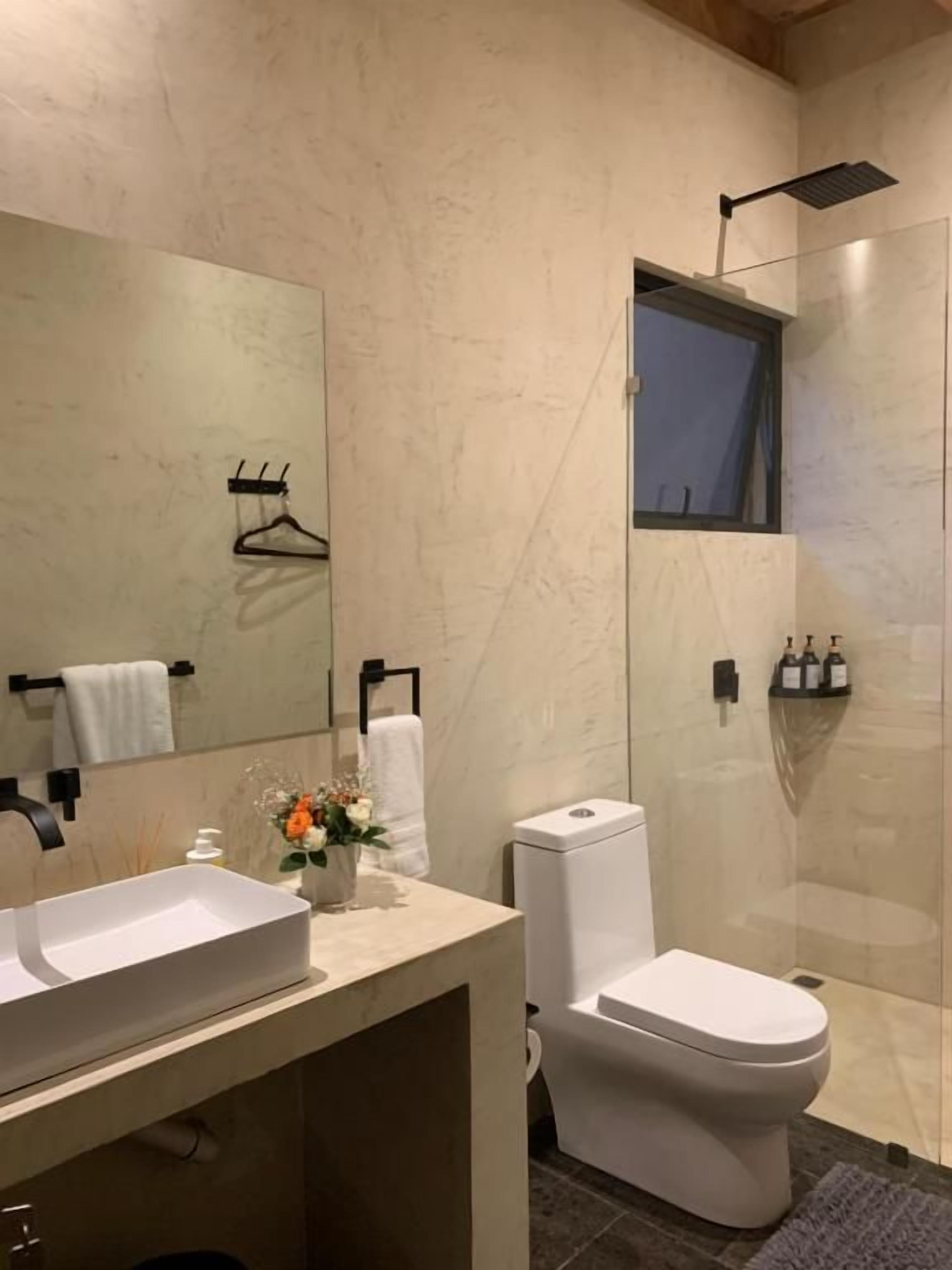 Un baño moderno con un espejo grande, inodoro y zona de ducha.