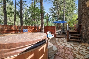 Ein Whirlpoolbereich mit einer Steinterrasse, umgeben von Bäumen, und einer Holzterrasse mit Gartenmöbeln.