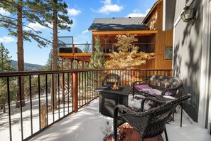 A balcony with a fire pit, wicker furniture, and a view of a mountain. - Wondrous Juniper House (Big Bear Lake)
