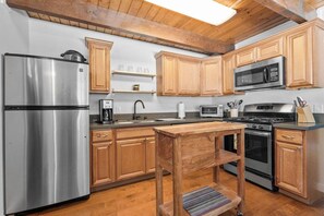 A kitchen with wooden cabinets, stainless steel appliances, and a wooden table. - Wondrous Juniper House (Big Bear Lake)
