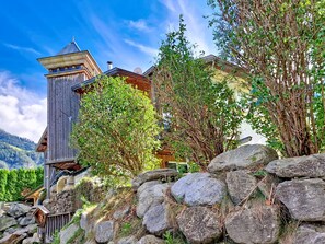 A rustic wooden building with a tower, surrounded by lush greenery and a stone wall.