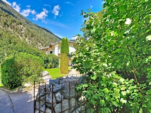 Una casa de muntanya amb mur de pedra, jardí i cel serè.