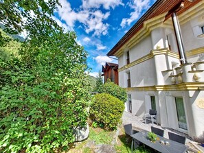 A building with a balcony, a table with chairs, and a garden area with greenery.