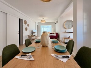 Een eetgedeelte met een houten tafel, groene stoelen en een rode bank op de achtergrond.